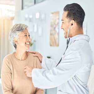 Male doctor listening to a females heart rate using a stethescope.