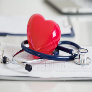 Red plastic heart on top of ekg results and a stethescope.